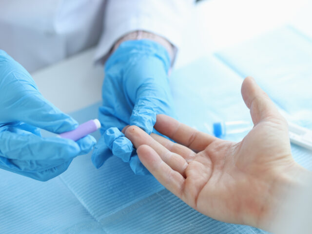 Gloved doctor takes blood test with lancet from patient at clinic